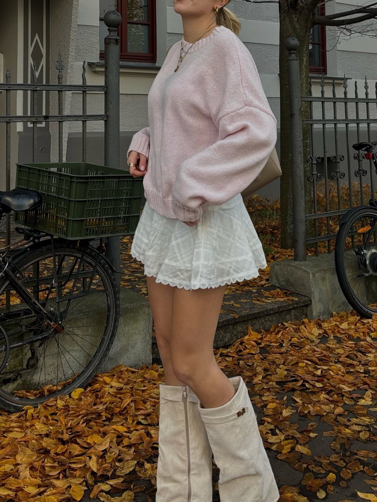 A person wearing a pink knit sweater, white mini skirt, and tall cream boots.