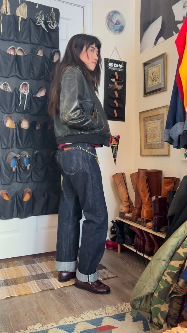 Woman wearing a dark leather jacket and wide-leg denim jeans standing in a room.