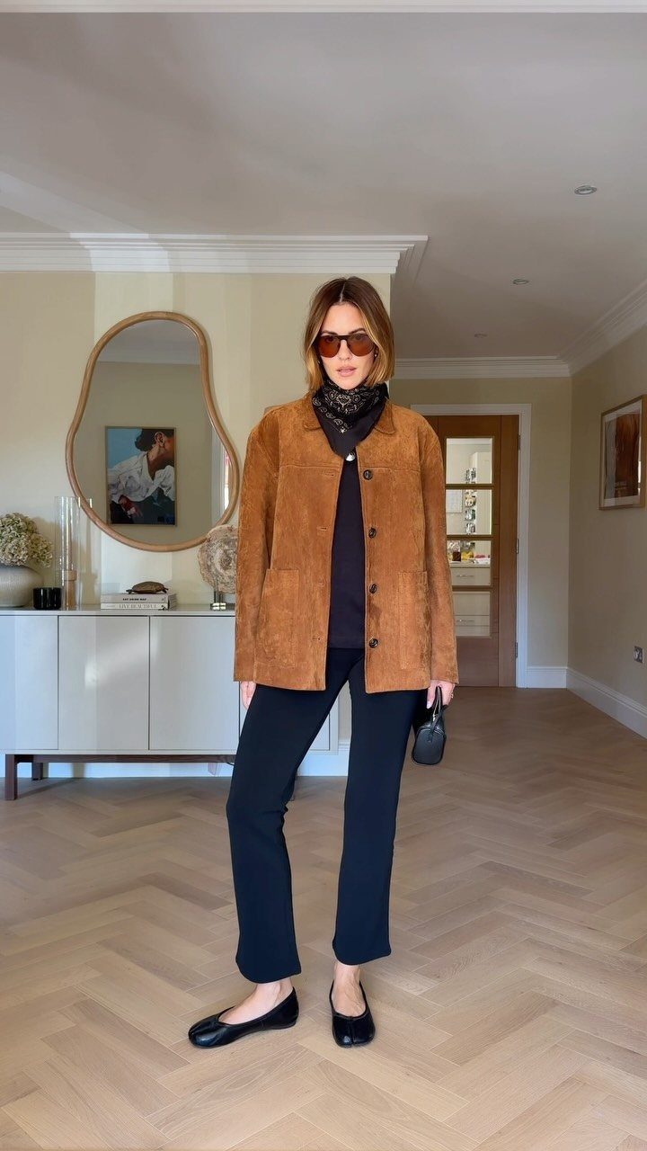 Woman wearing a brown suede jacket, black top, black trousers, and black ballet flats.