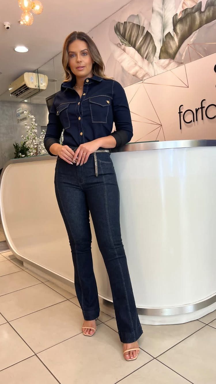 Woman wearing a dark denim jumpsuit with flared boot-cut legs standing indoors.
