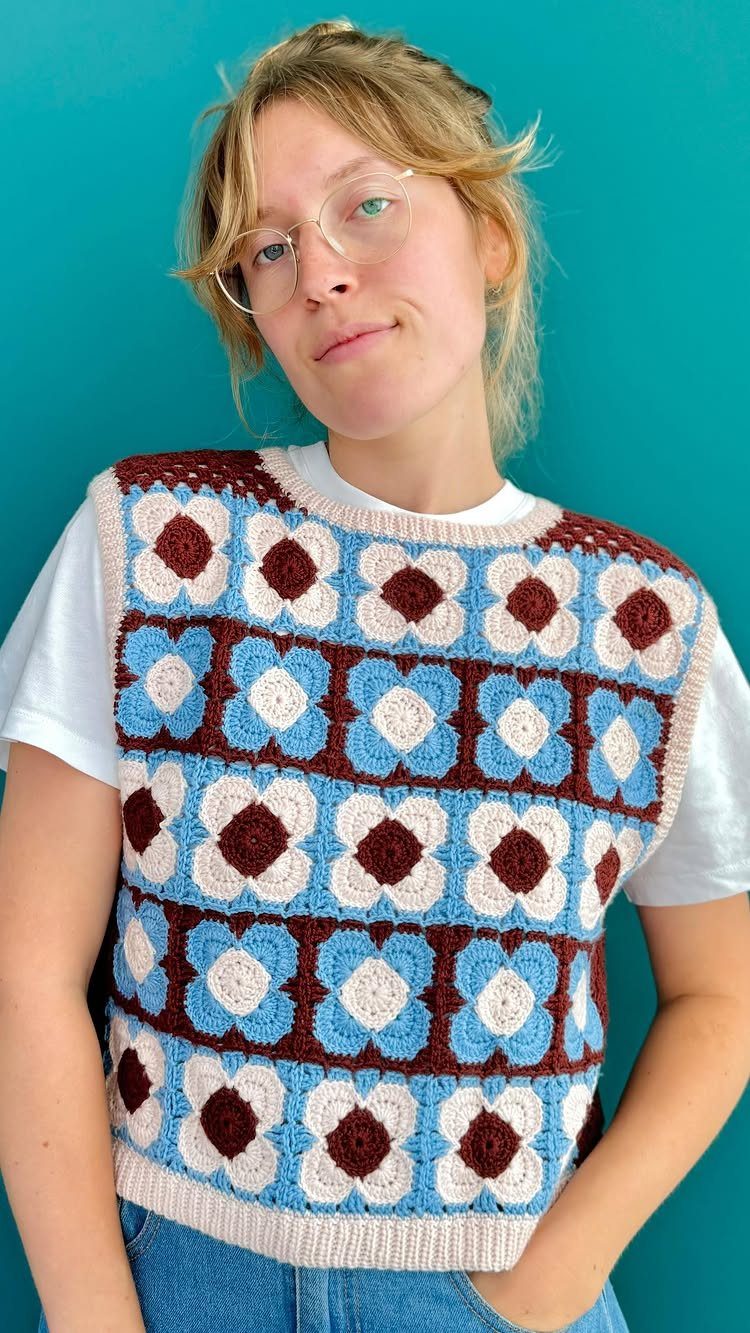 A person wearing a blue and brown crocheted floral pattern sweater vest over a white t-shirt.