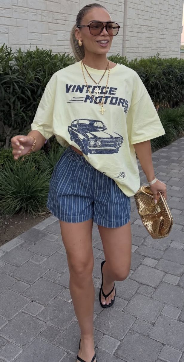 A woman in a yellow graphic t-shirt and striped shorts walking outdoors.