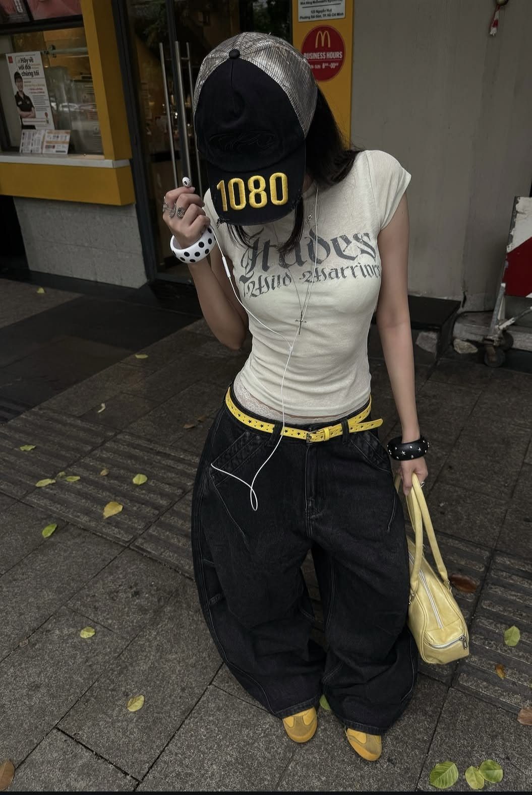 Person in streetwear wearing baggy black pants, a graphic tee, and a silver baseball cap.