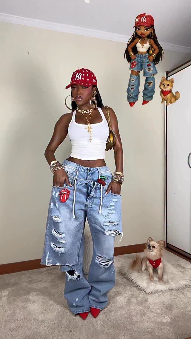 Woman wearing oversized distressed denim jeans, a white crop top, and a red cap posing indoors.