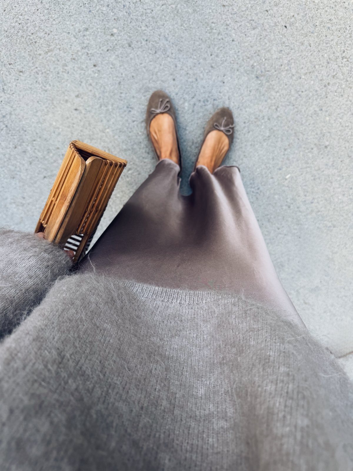 Person wearing grey wide-leg trousers, brown ballet flats, and a grey sweater standing on concrete.