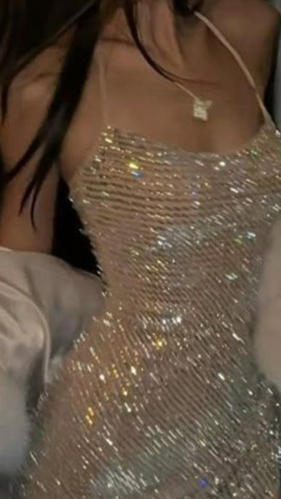 A person wearing a sparkling, silver sequined mini dress with thin straps and a gold necklace.
