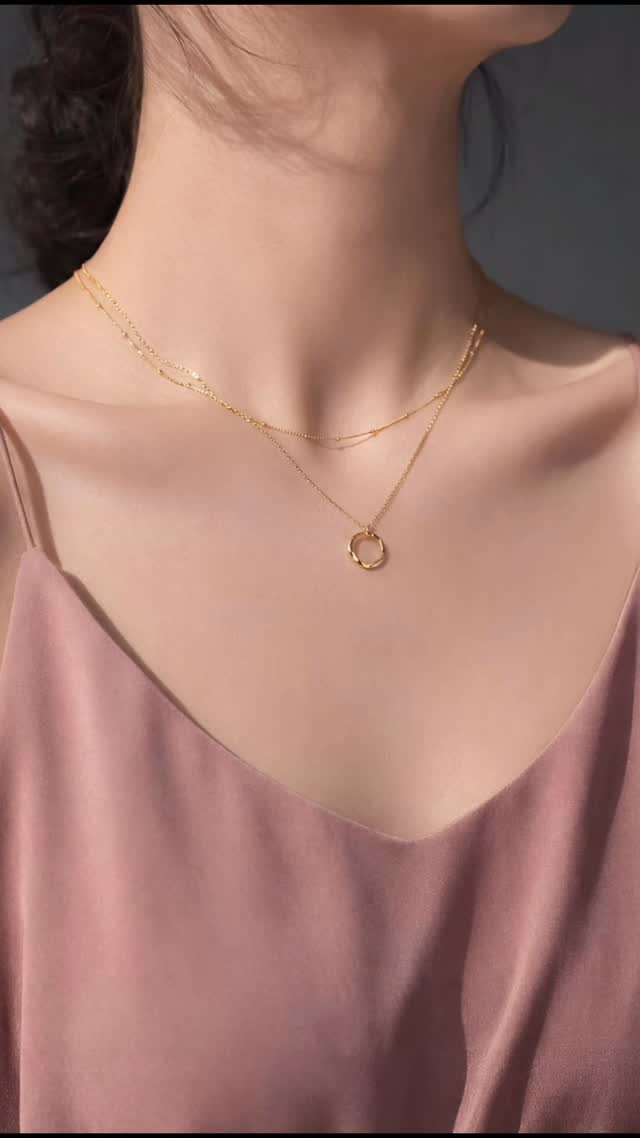 Two delicate gold necklaces with a circular pendant worn on a person's neck.