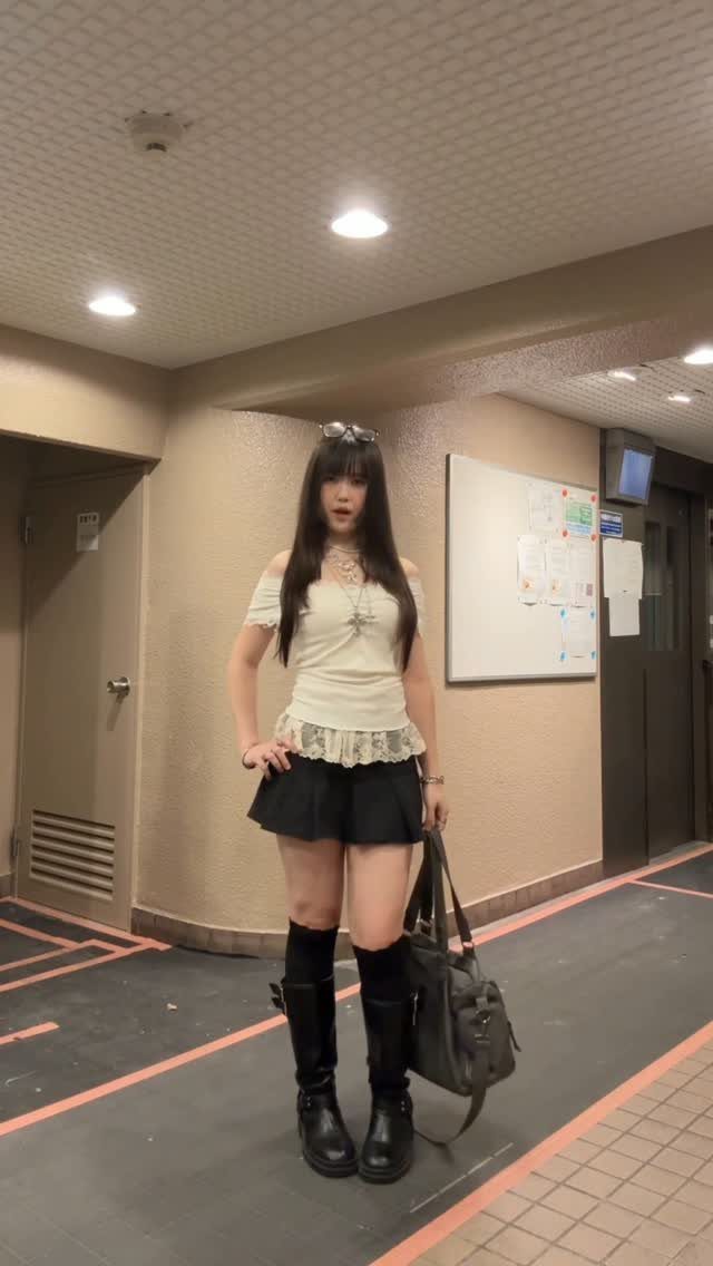 A woman posing in a cream top, black mini skirt, and tall black boots.