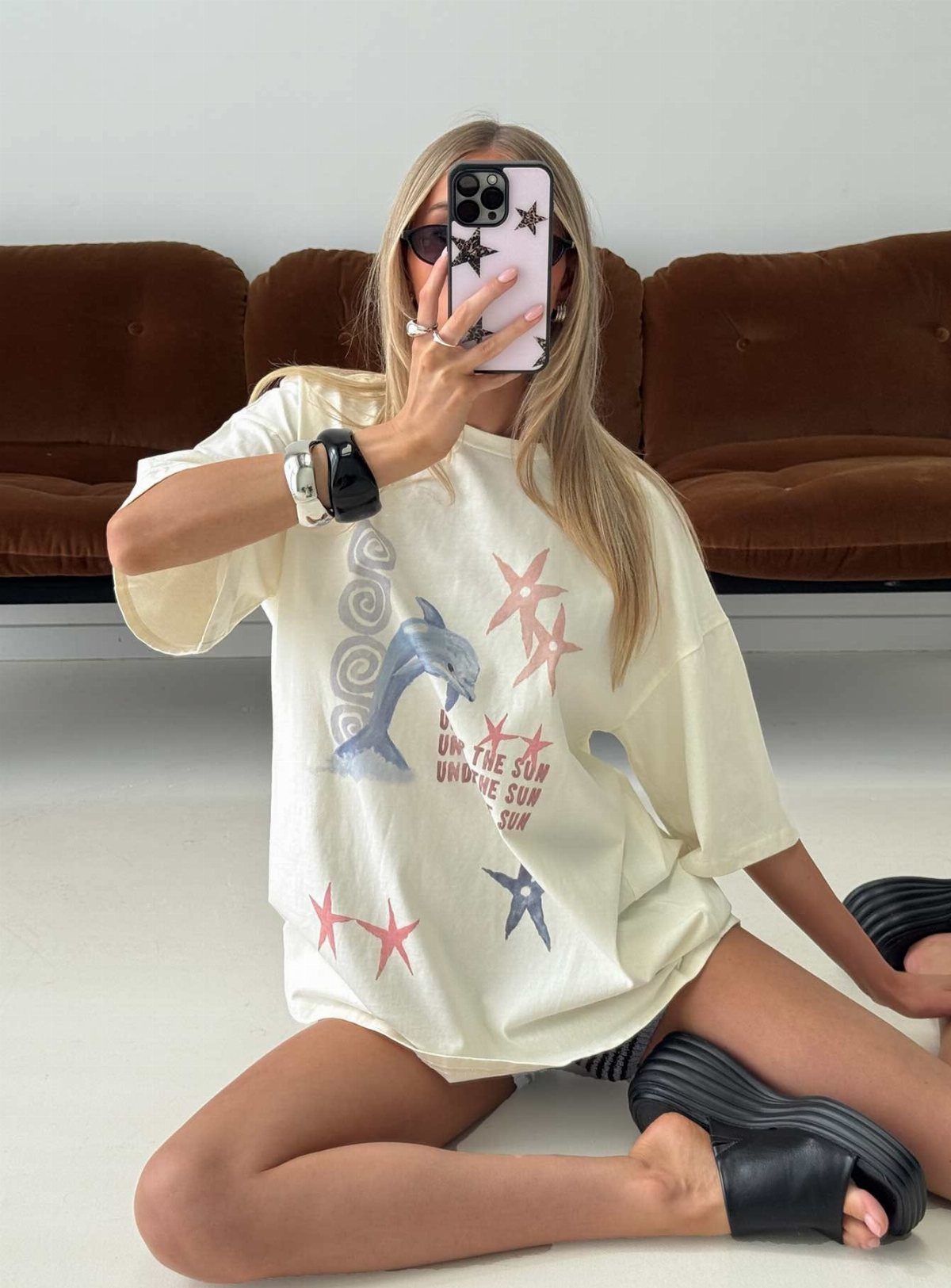 A woman sitting on the floor wearing an oversized cream graphic t-shirt with a dolphin print.