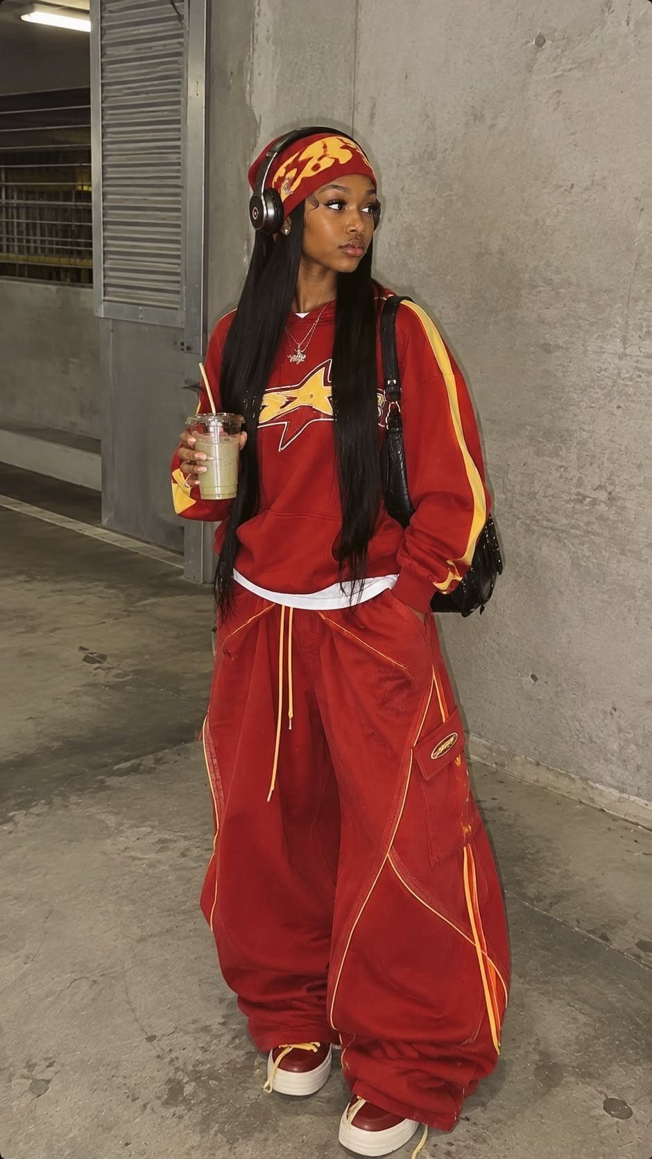 A woman in red streetwear outfit posing in an urban concrete setting.