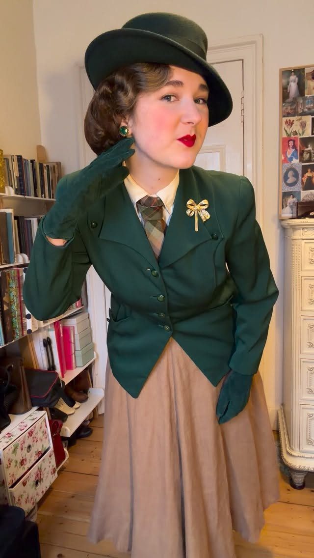 A woman posing in a vintage green jacket, matching hat, gloves, and a long tan skirt.