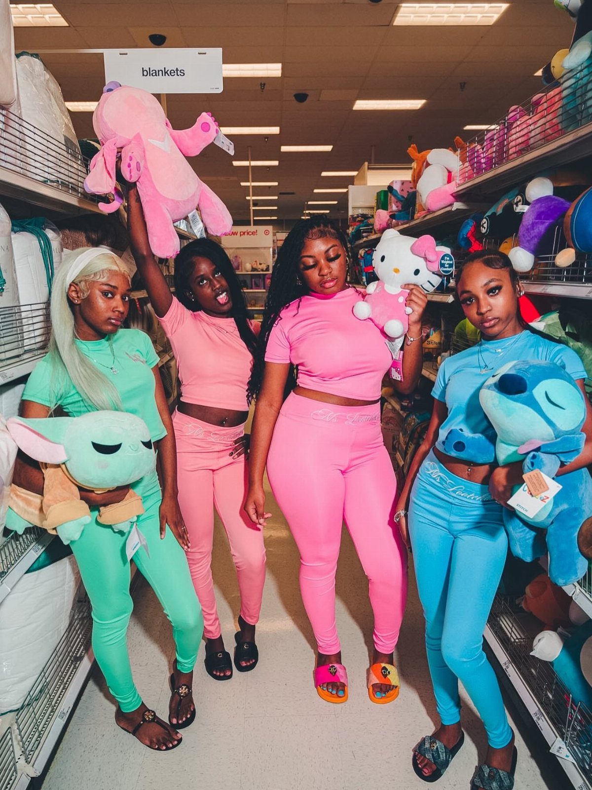 Four women posing in a store aisle wearing colorful coordinated athleisure sets while holding plush toys.