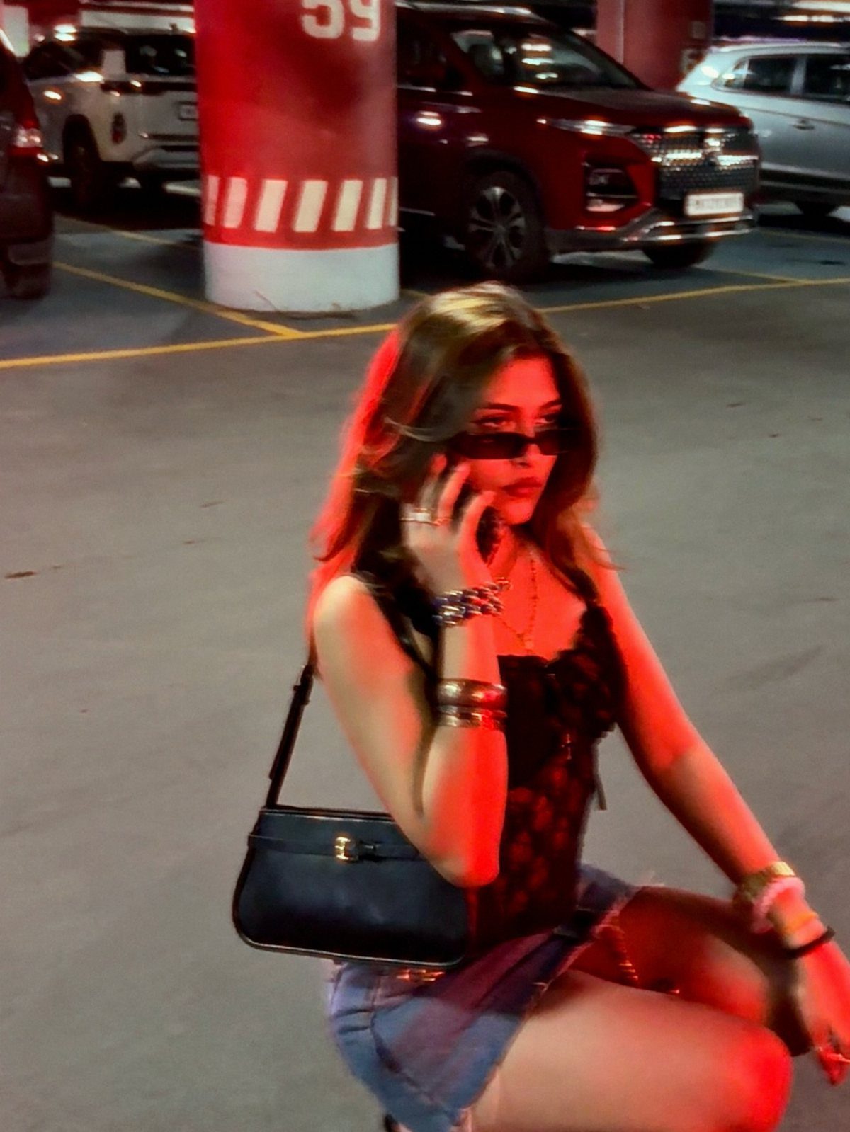 A woman in sunglasses and a black top posing in a red-lit parking garage.