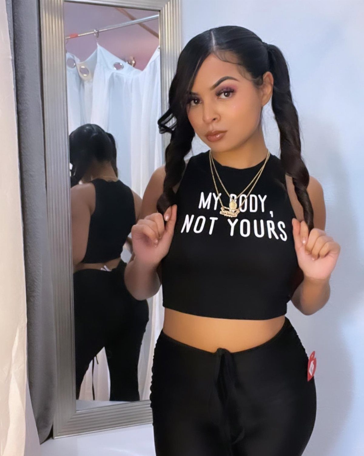 A woman in a black cropped halter top and black pants posing in front of a mirror.