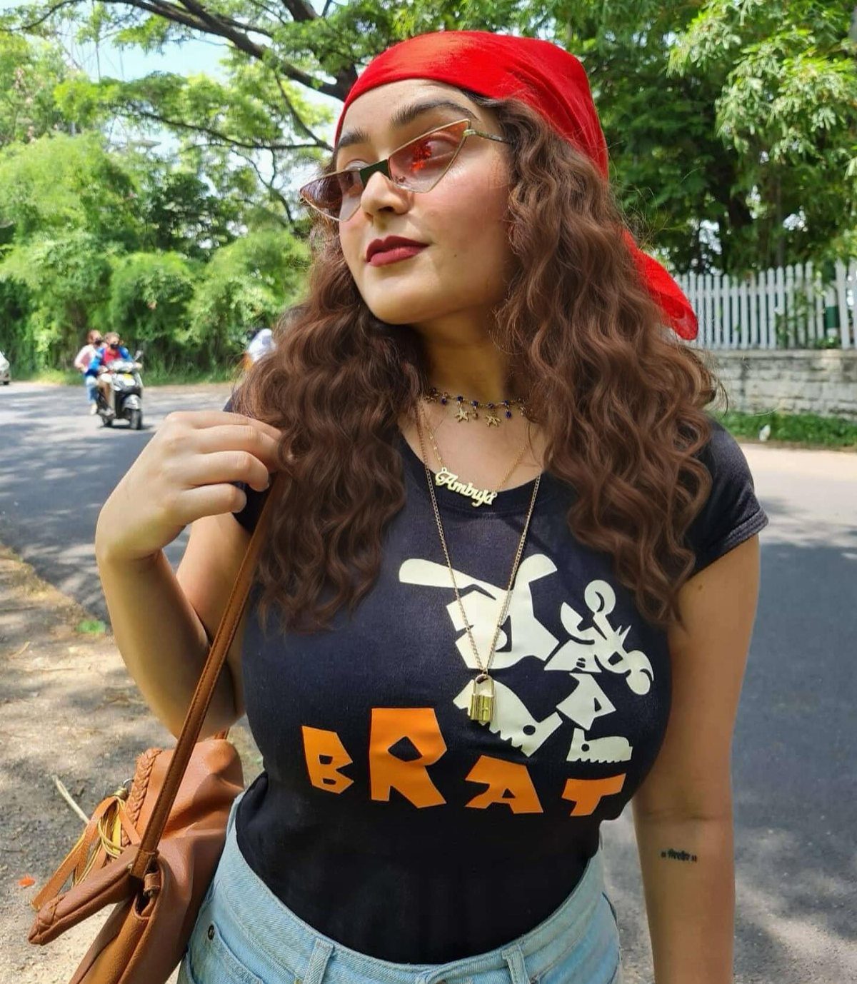 A woman wearing a red bandana, sunglasses, and a black graphic t-shirt posing outdoors.