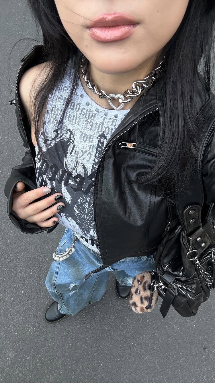A person wearing a black leather jacket, graphic tank top, and a chunky silver chain necklace.