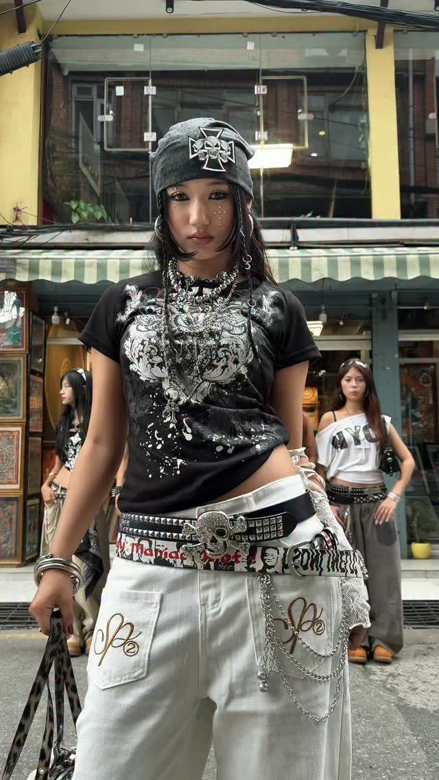 Young woman in a black graphic crop top and white baggy trousers with silver chains.