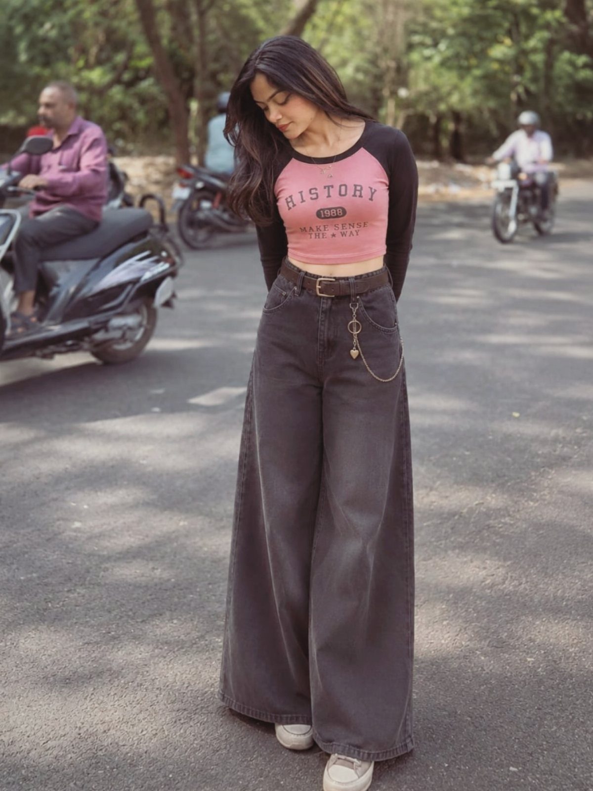 Woman wearing a pink graphic cropped top and dark baggy wide-leg jeans standing on a street.