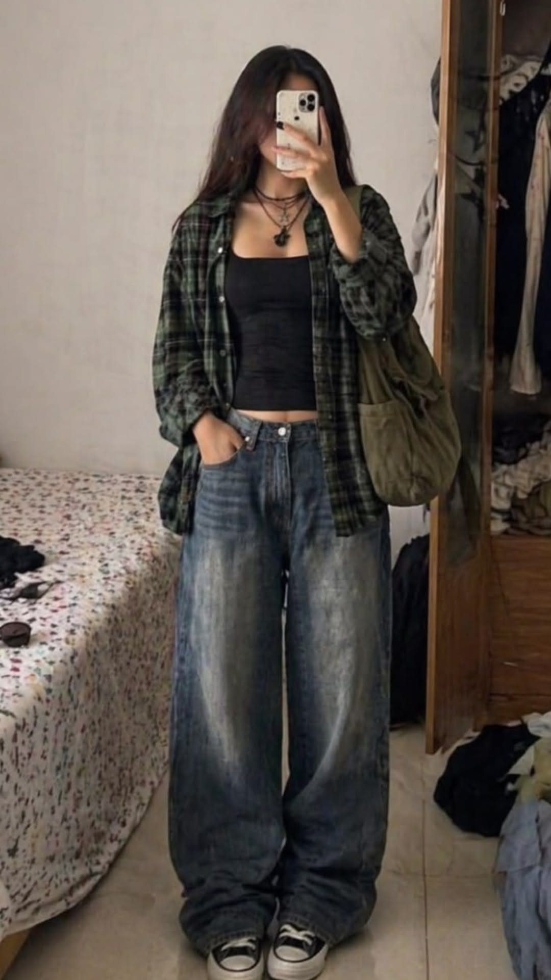 A person posing in a dark green flannel shirt, black tank top, and baggy blue jeans.