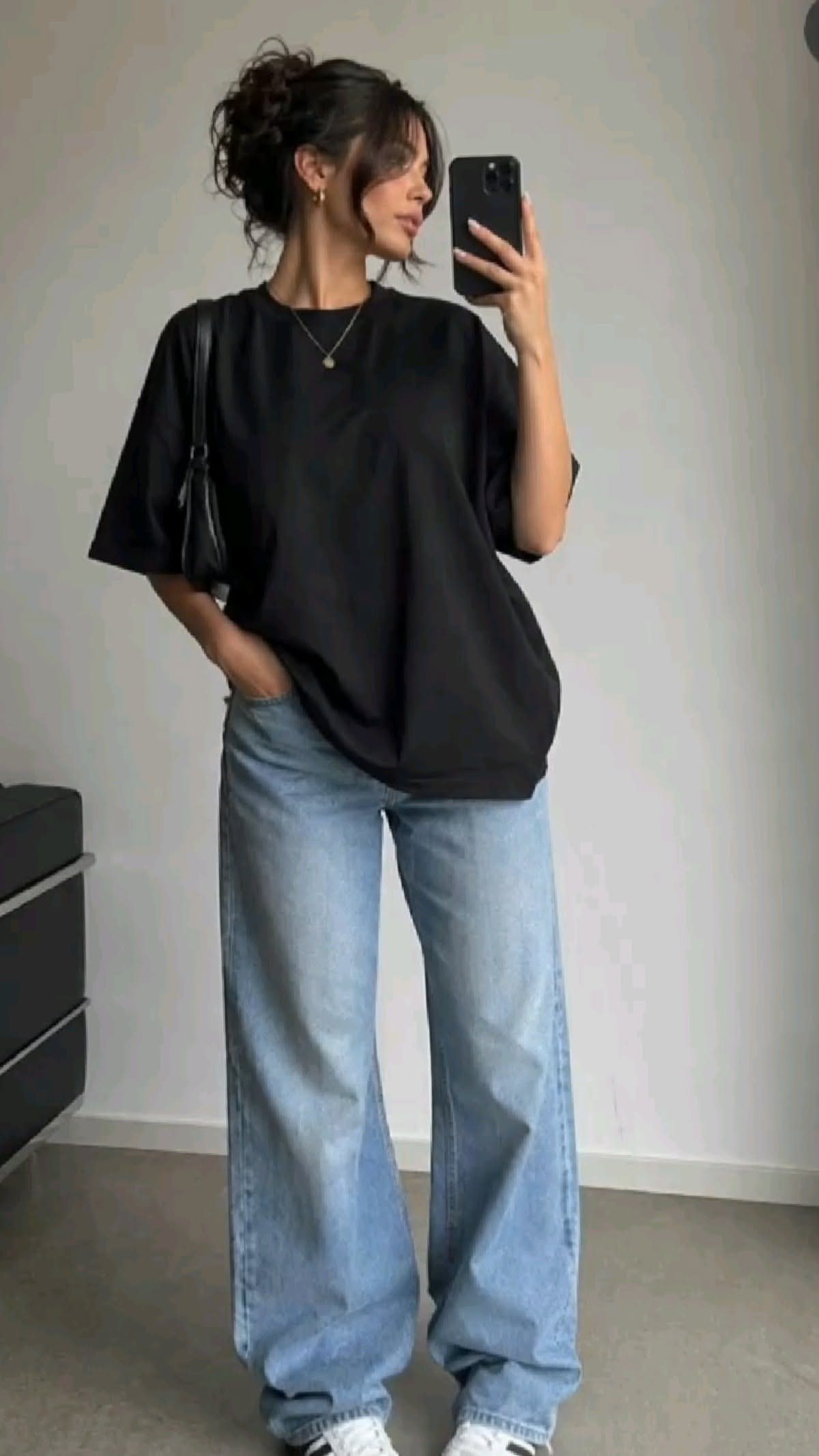 Woman in an oversized black t-shirt and baggy light blue jeans taking a mirror selfie.