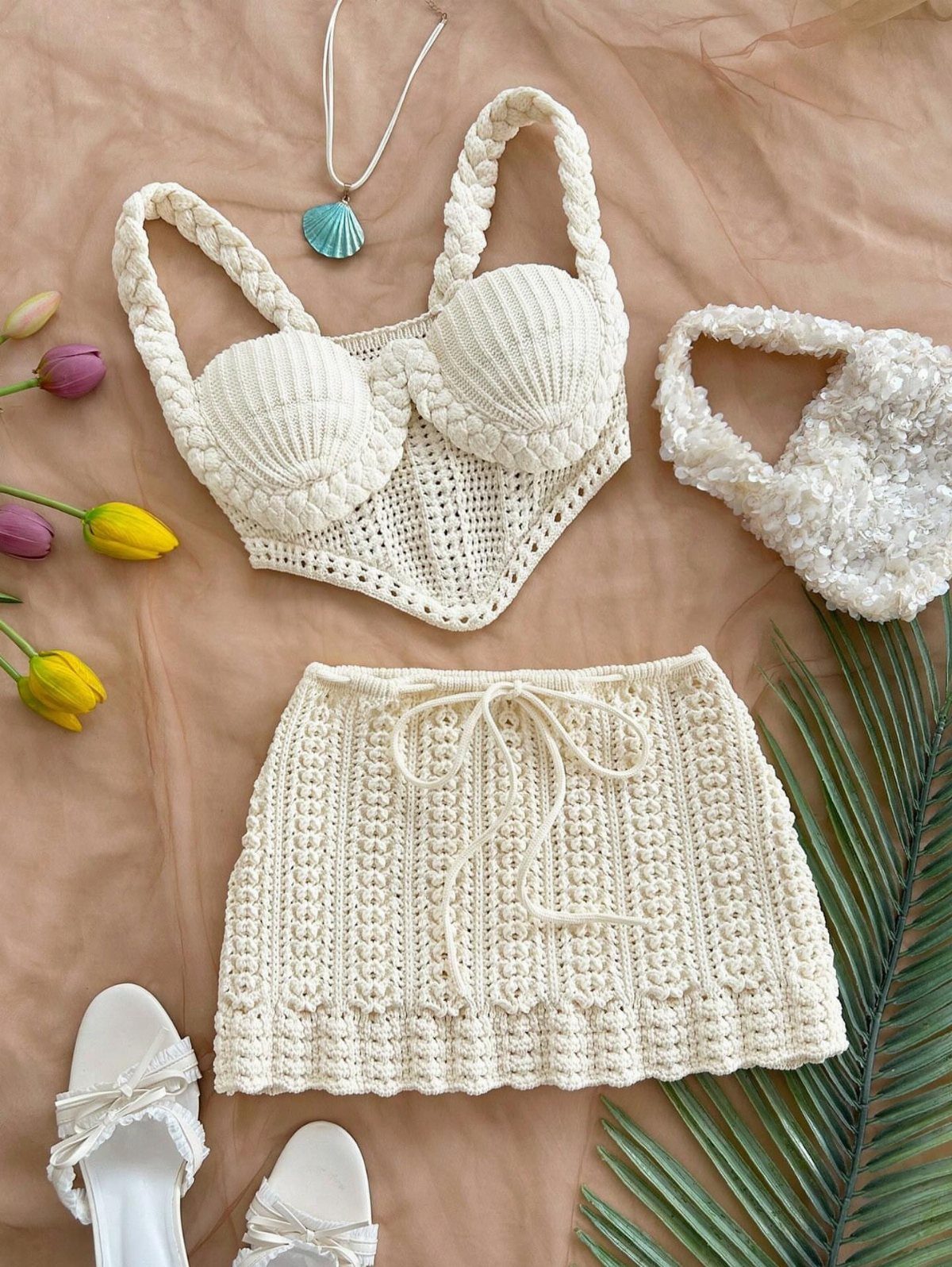 Cream crochet knit bra top and matching mini skirt laid on tan fabric with accessories.