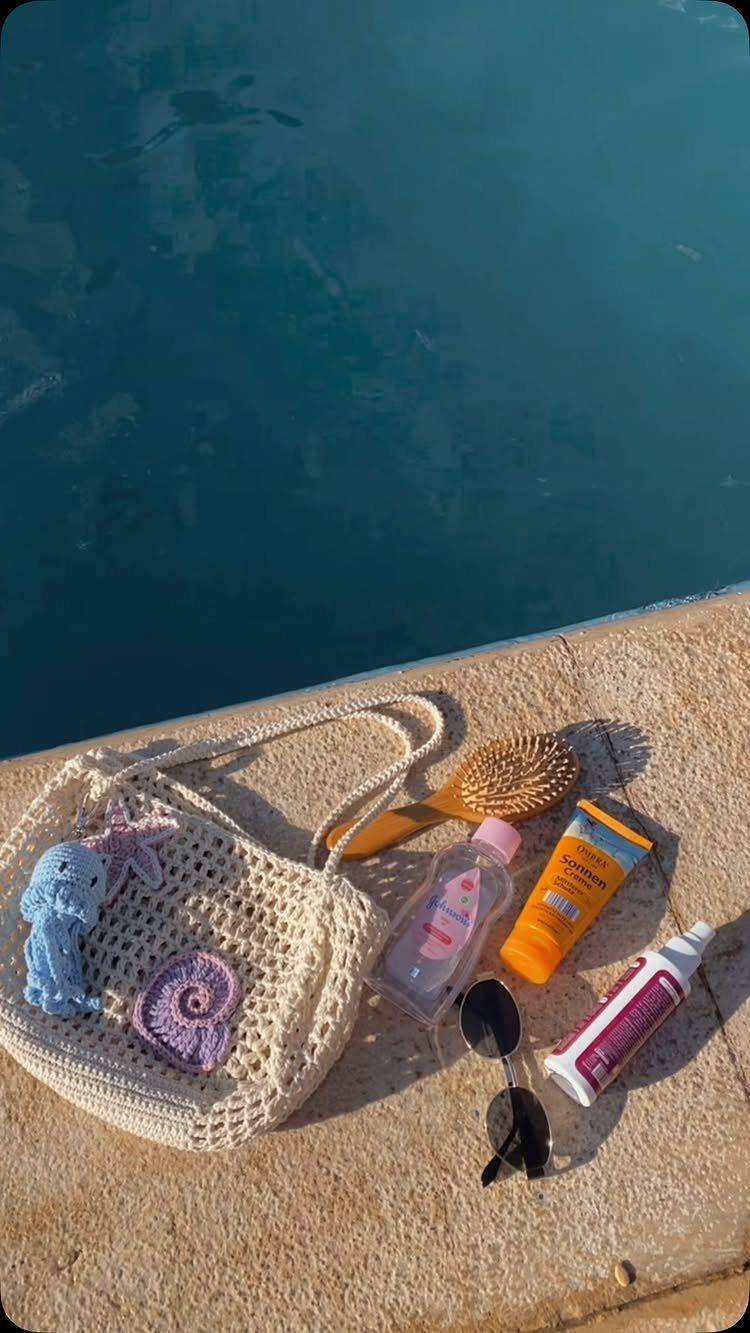 Cream crochet tote bag resting on a stone ledge next to pool accessories.