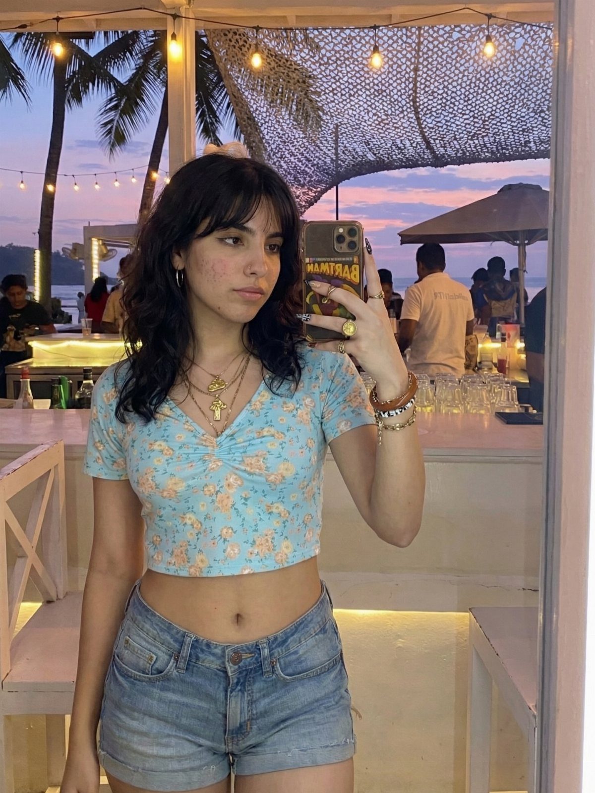 Woman in a light blue floral print crop top and denim shorts taking a selfie.
