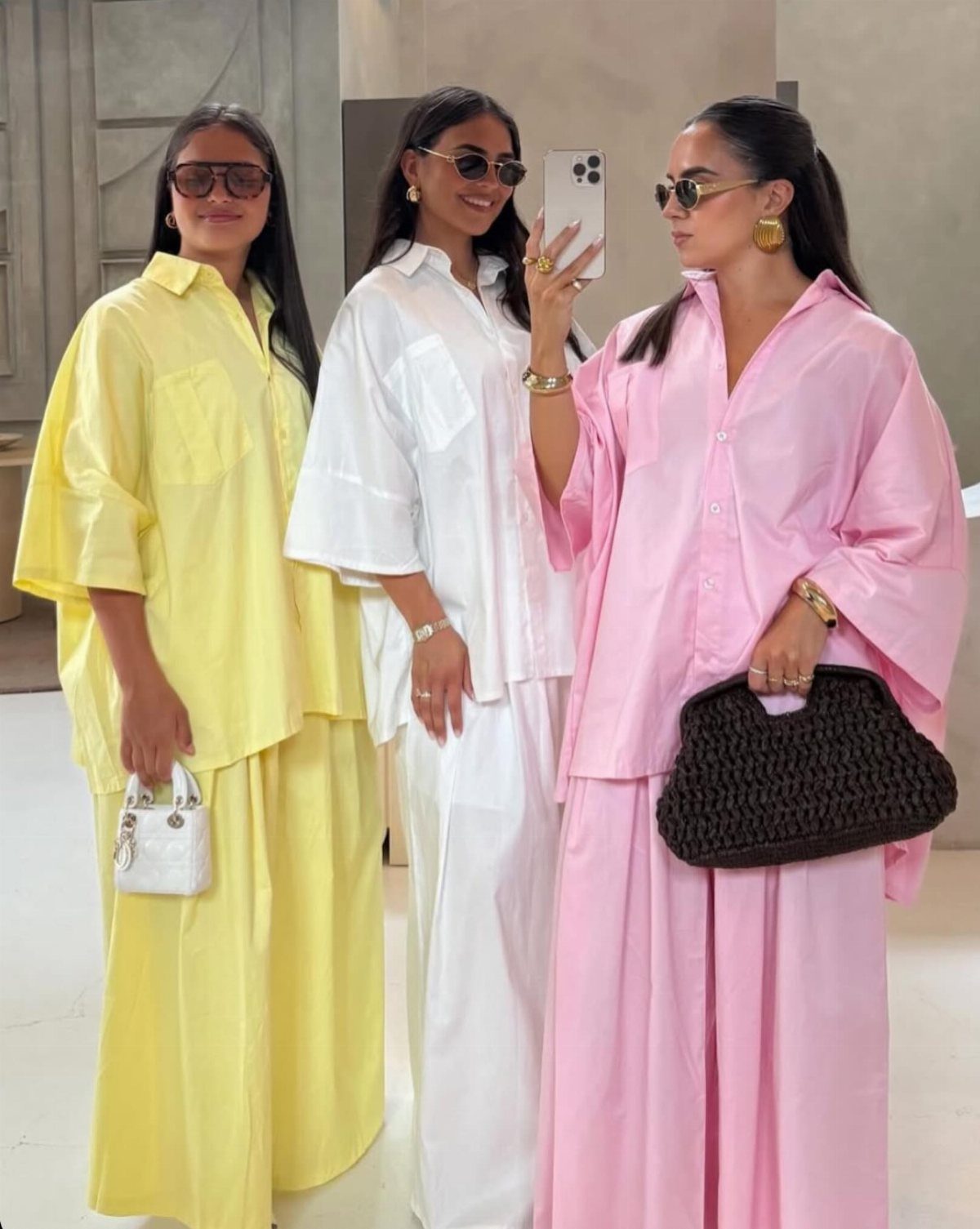 Three women posing in colorful oversized pastel shirts and matching long skirts.