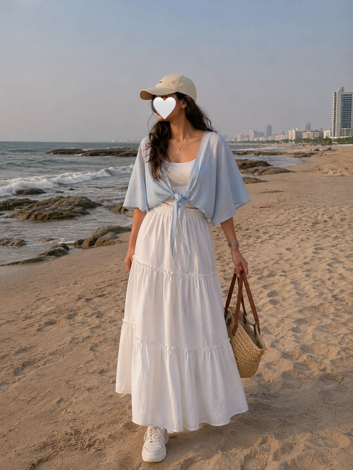 Woman in a white tiered maxi skirt and blue top walking along a sandy beach.