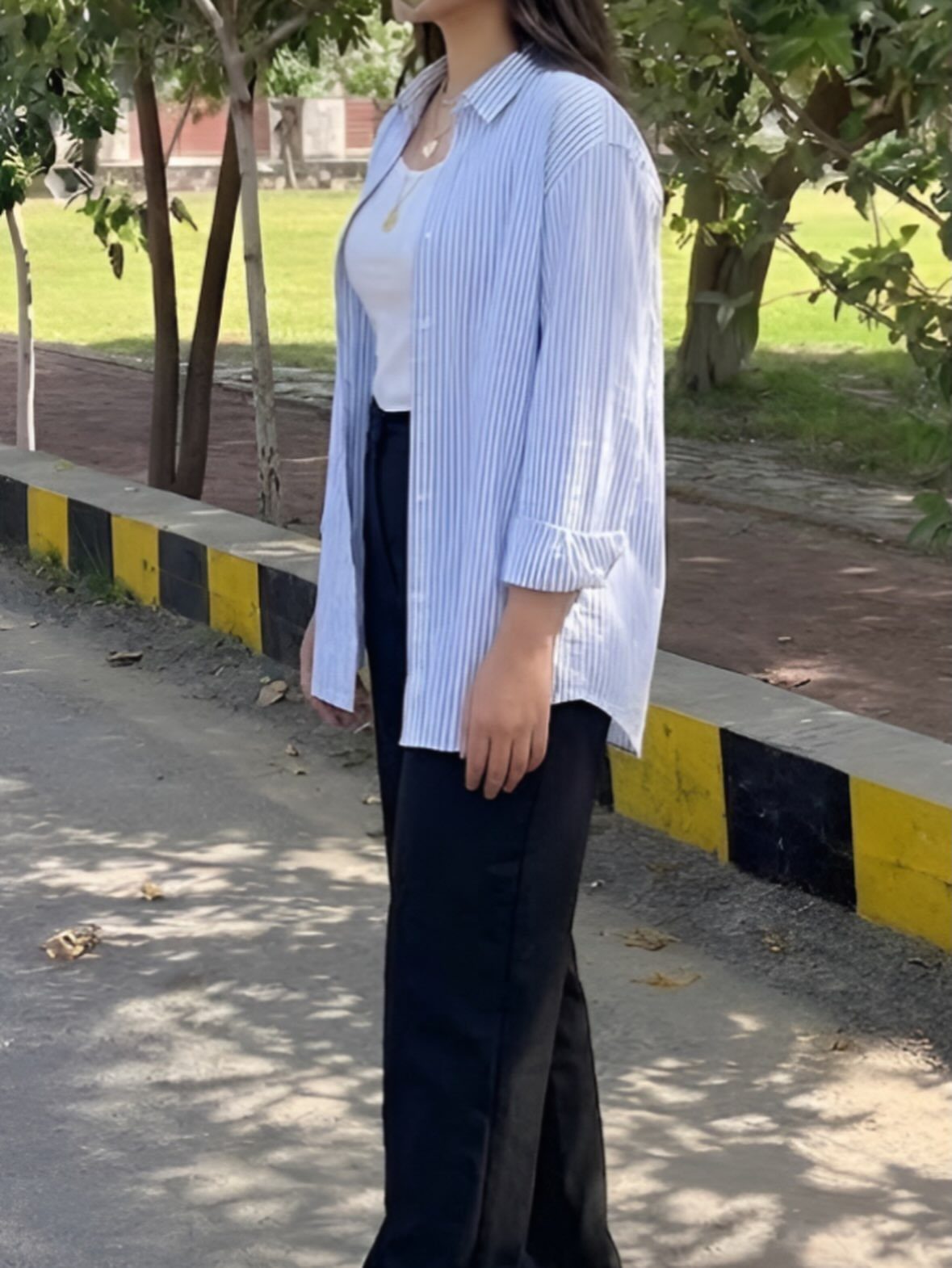 A person wearing black wide-leg trousers and an unbuttoned striped shirt outdoors.