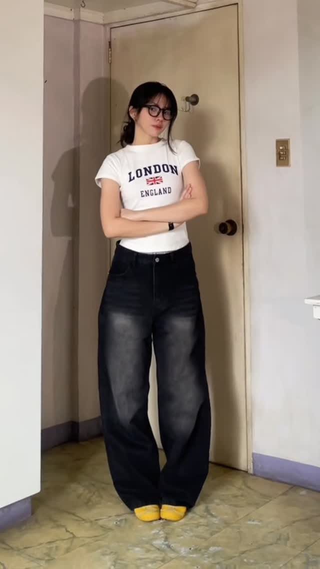 A woman posing in a white graphic t-shirt, wide-leg black jeans, and yellow shoes.