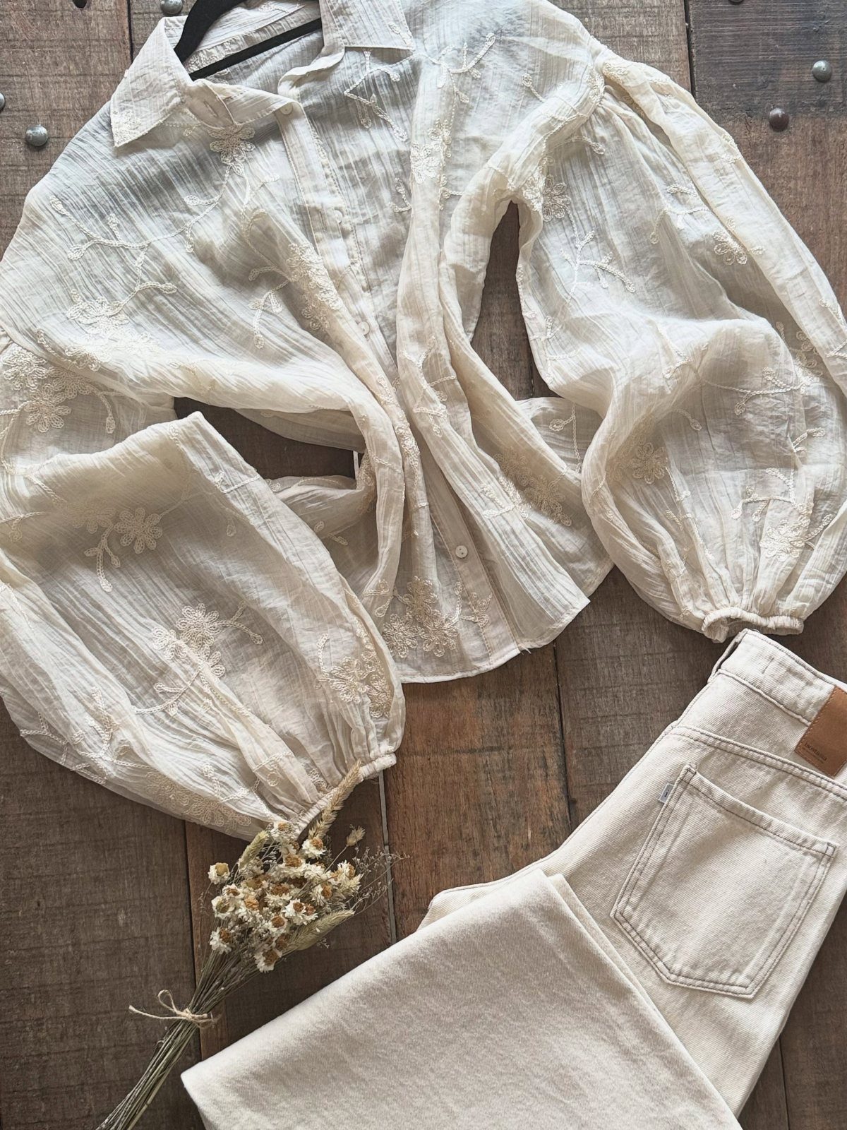 Cream embroidered flowy blouse and matching denim jeans on a rustic wooden surface.