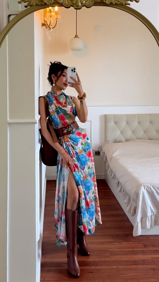 Woman in a colorful floral midi dress and brown boots posing for a mirror selfie.