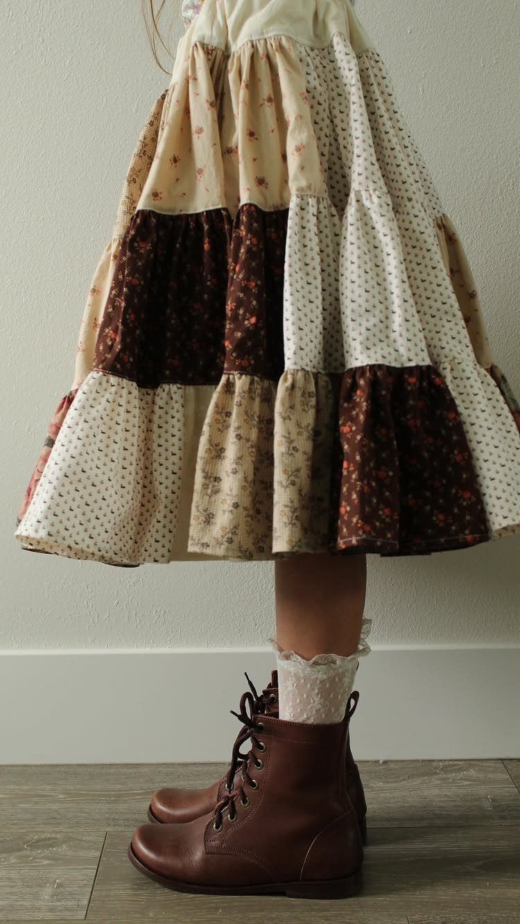 A person wearing a patchwork tiered skirt with brown leather boots and lace socks.