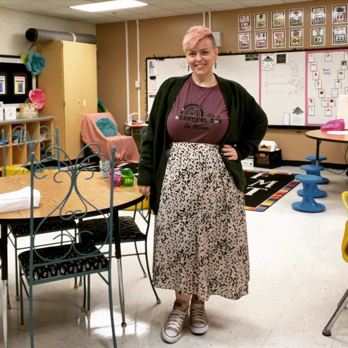 A woman wearing a dark green cardigan over a maroon graphic t-shirt and patterned skirt.