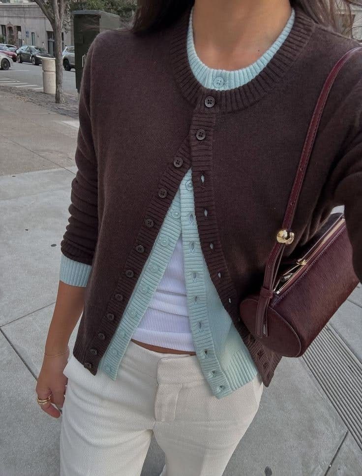 A person wearing a dark brown cardigan layered over a light blue cardigan and white top.