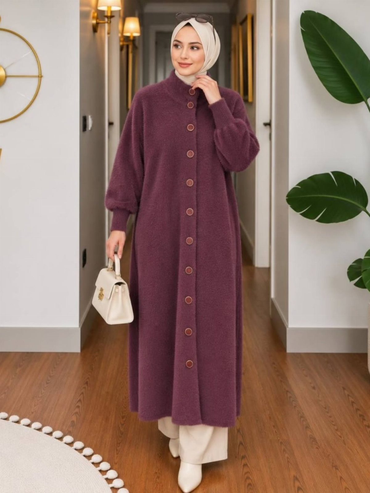 A woman in a long purple cardigan and white trousers walking through a hallway.