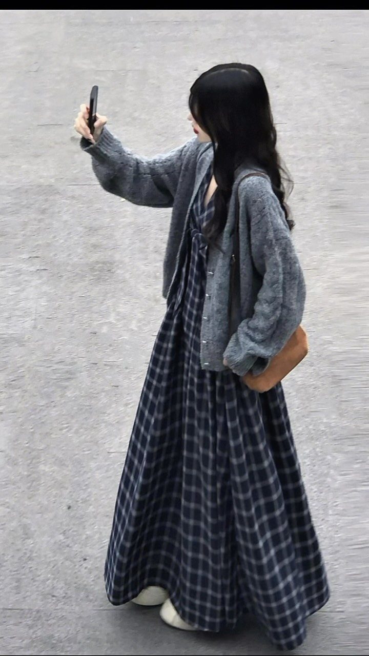 A woman in a grey cardigan and navy plaid maxi skirt taking a selfie outdoors.