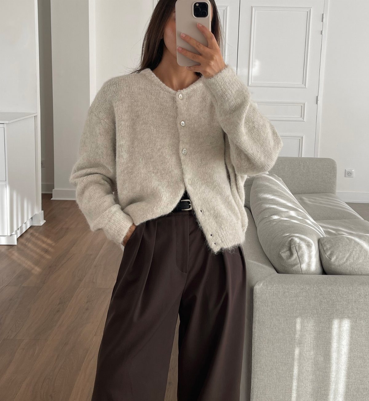 Person wearing a cream fuzzy cardigan and dark brown wide-leg trousers taking a mirror selfie.