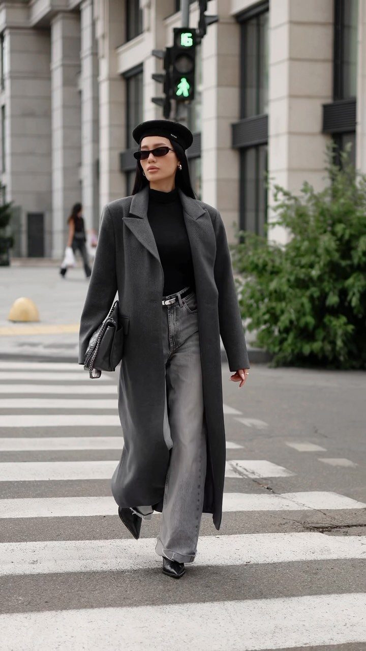 Woman in a long grey wool coat and black beret walking across a city street.