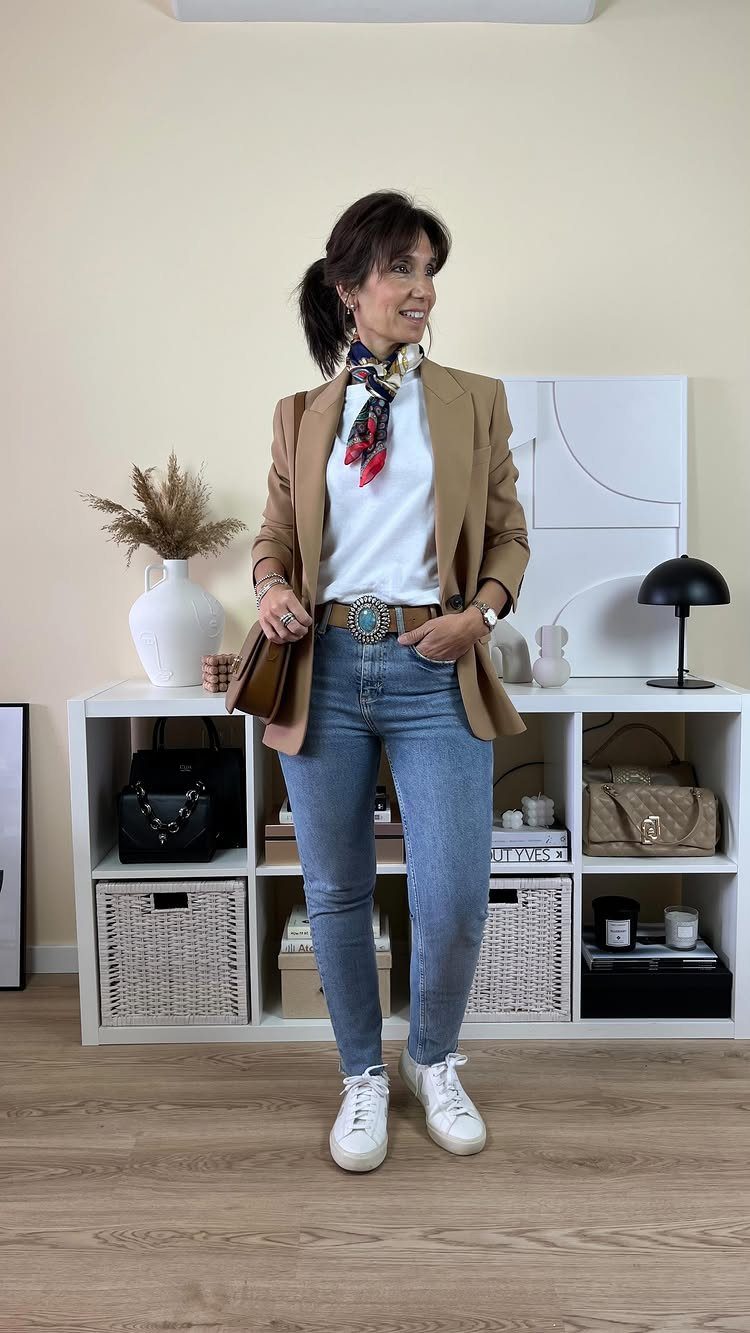 A woman wearing a tan blazer, blue jeans, and a colorful patterned neck scarf.