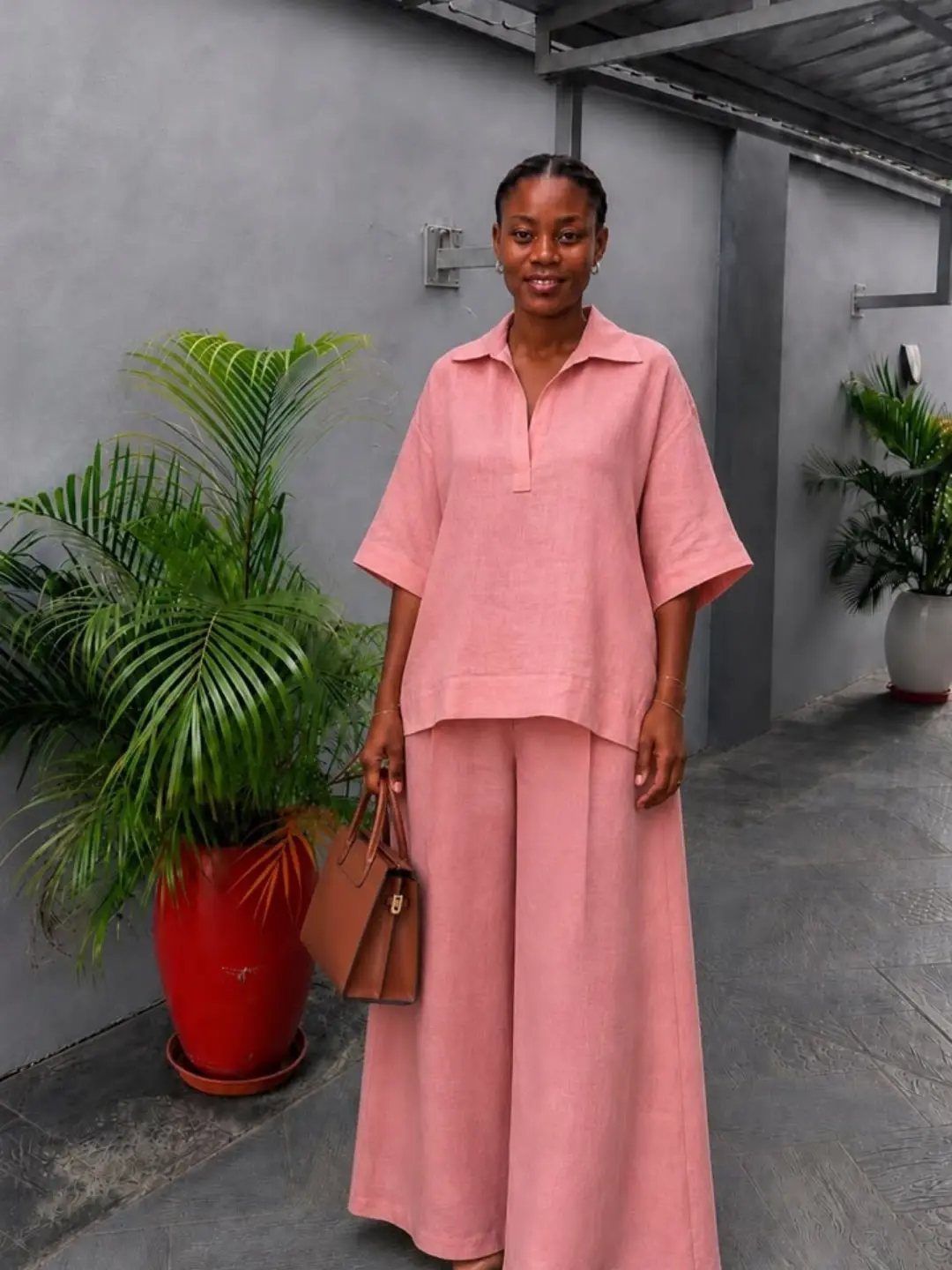 Woman wearing a pink linen shirt and matching wide-leg trousers holding a brown handbag.