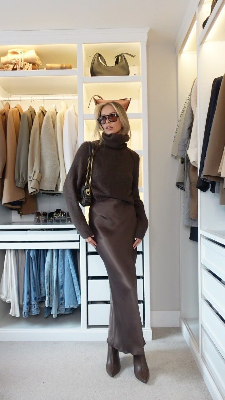 Woman in a brown turtleneck and satin skirt posing in a white walk-in closet.