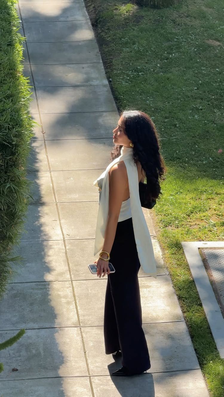A woman in a white halter top and black wide-leg trousers walking on a path.