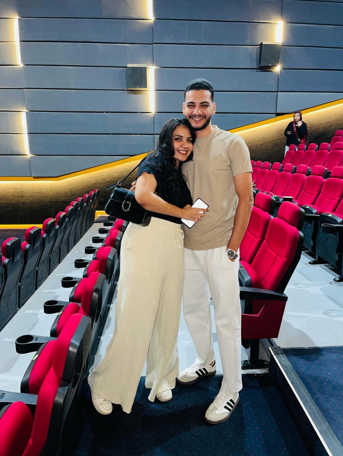 A smiling couple posing for a photo inside a movie theater with red seats.