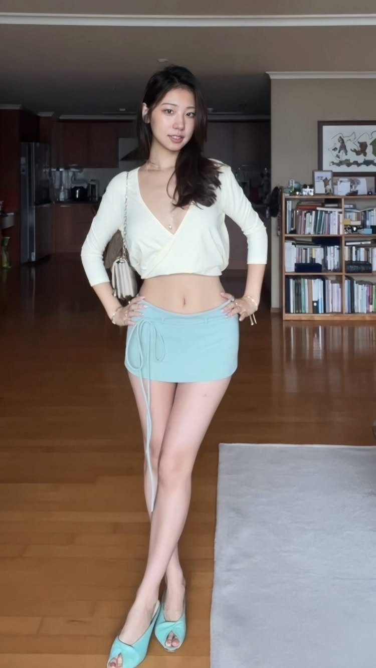 A woman posing in a cream wrap top, light blue mini skirt, and matching heels.