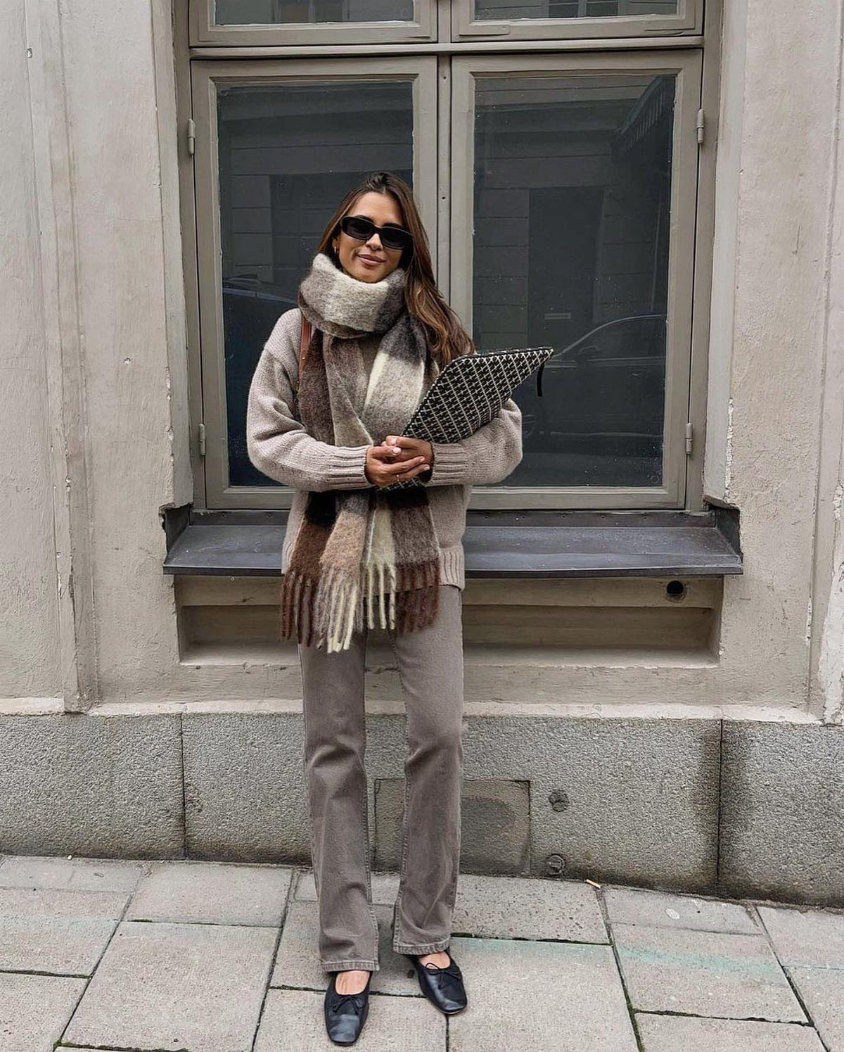 A woman wearing a beige sweater and a large, chunky knit scarf with fringe details.