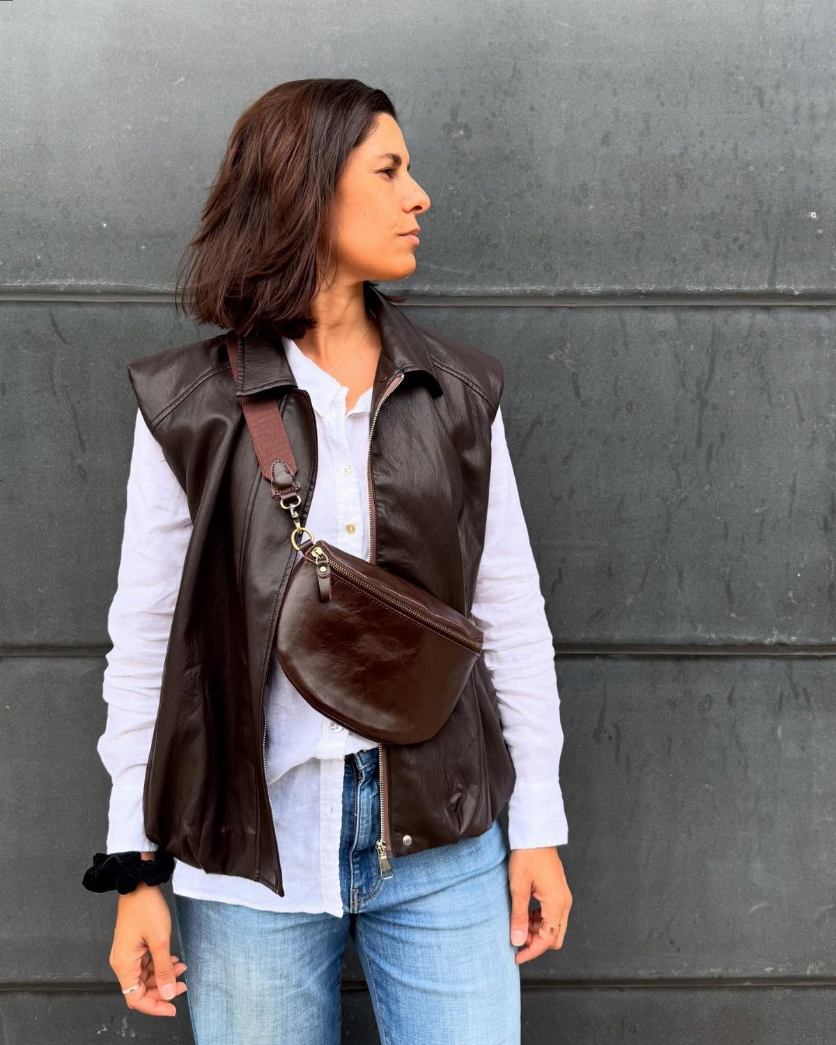 Woman wearing a white shirt, blue jeans, and a dark brown leather crossbody bag.
