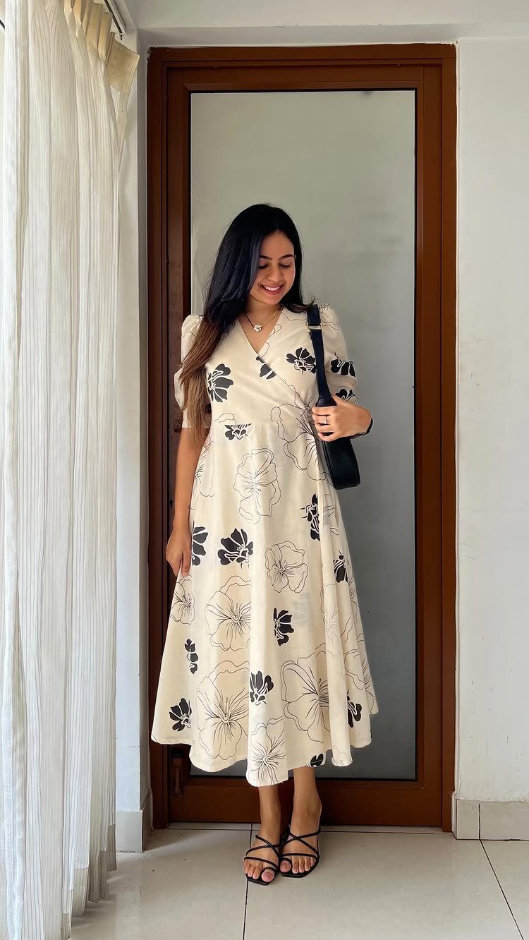 A woman wearing a cream floral wrap dress and black sandals standing in front of a mirror.