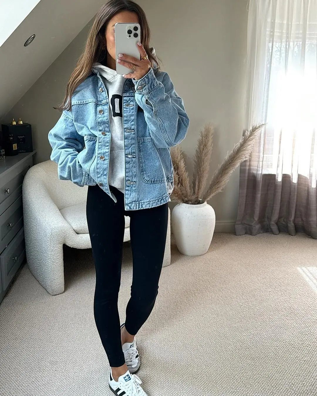 A woman posing in a mirror wearing a light blue denim jacket and black leggings.